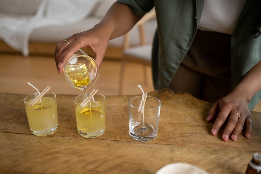A person pours wax into glass jars for candle making, showcasing a hands-on small business craft.